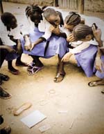 A group of young women seated on a bench discuss priorities whilst looking at everyday objects lying on the ground in front of them.