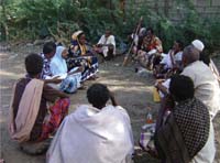 A small group of people are seated crossed leg on the ground in a circle.