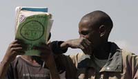Two students laughing together. One covers his face with a text book.