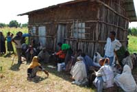 A group of peope gathered outside a hut.